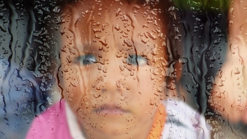 Trauriges Kind schaut durch eine verregnete Fensterscheibe